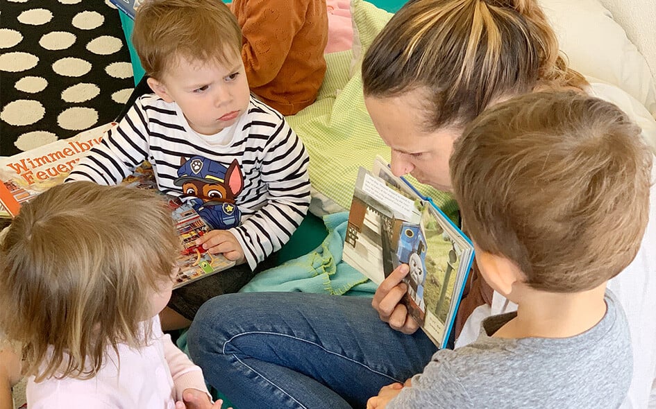 Eine Person zeigt drei Kindern ein Bilderbuch.