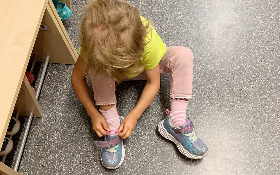 Ein Kind sitzt am Boden und zieht sich die Schuhe an.
