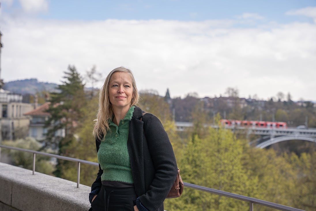 Camilla Landbø lehnt an einem Geländer. Im Hintergrund sieht man Bäume und eine Brücke.