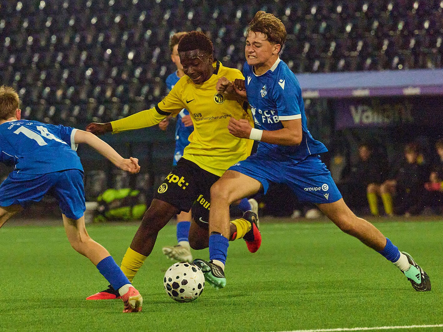 YB-Spieler im gelben Trikot kämpft mit zwei Gegenspielern in Blau um den Ball.