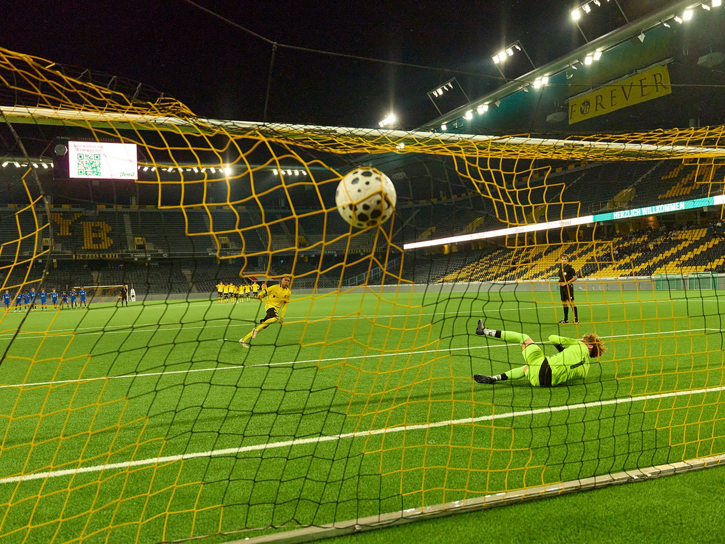 Fussball fliegt ins Tornetz, während der Torhüter am Boden liegt.