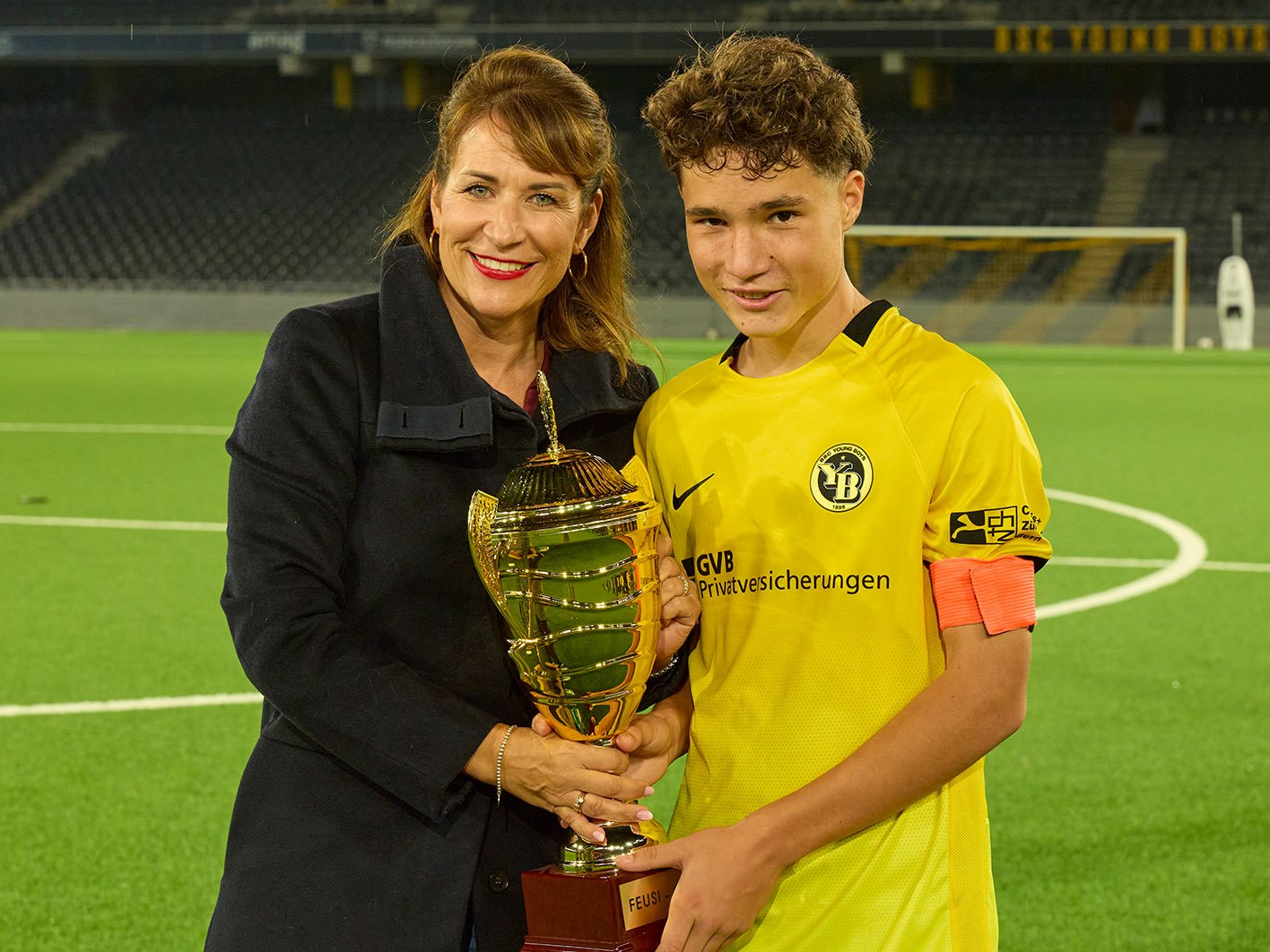 Frau und YB-Nachwuchsspieler präsentieren gemeinsam den goldenen Feusi-Cup-Pokal.