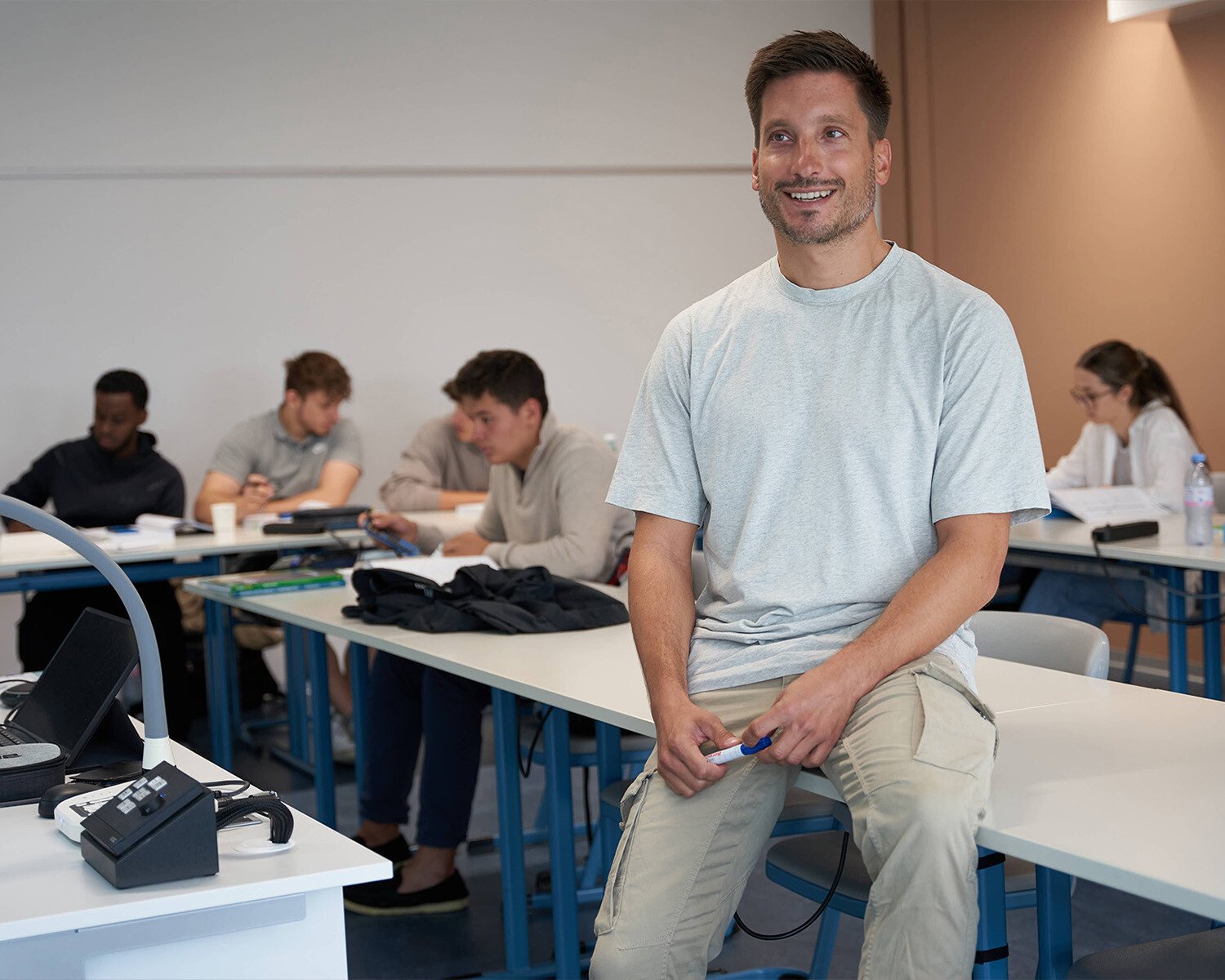 Im Vordergrund ein Mann. Im Hintergrund sitzen einige Schülerinnen und Schüler.