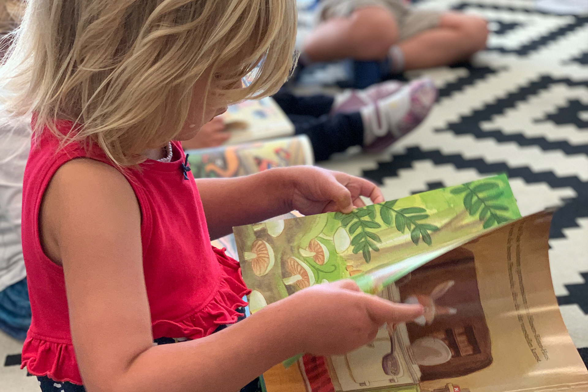 Kinder sitzen am Boden und schauen sich ein Bilderbuch an.