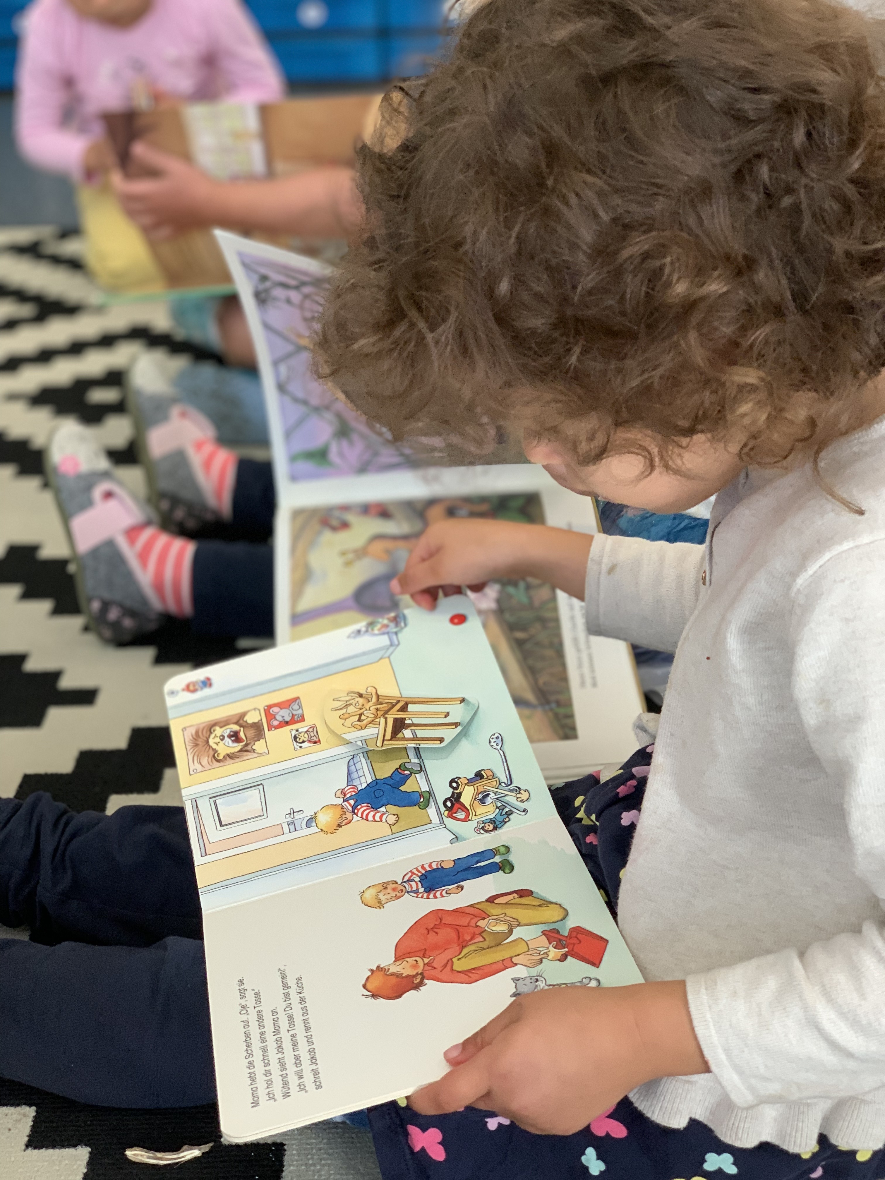 Kinder sitzen auf dem Boden und schauen sich ein Bilderbuch an.