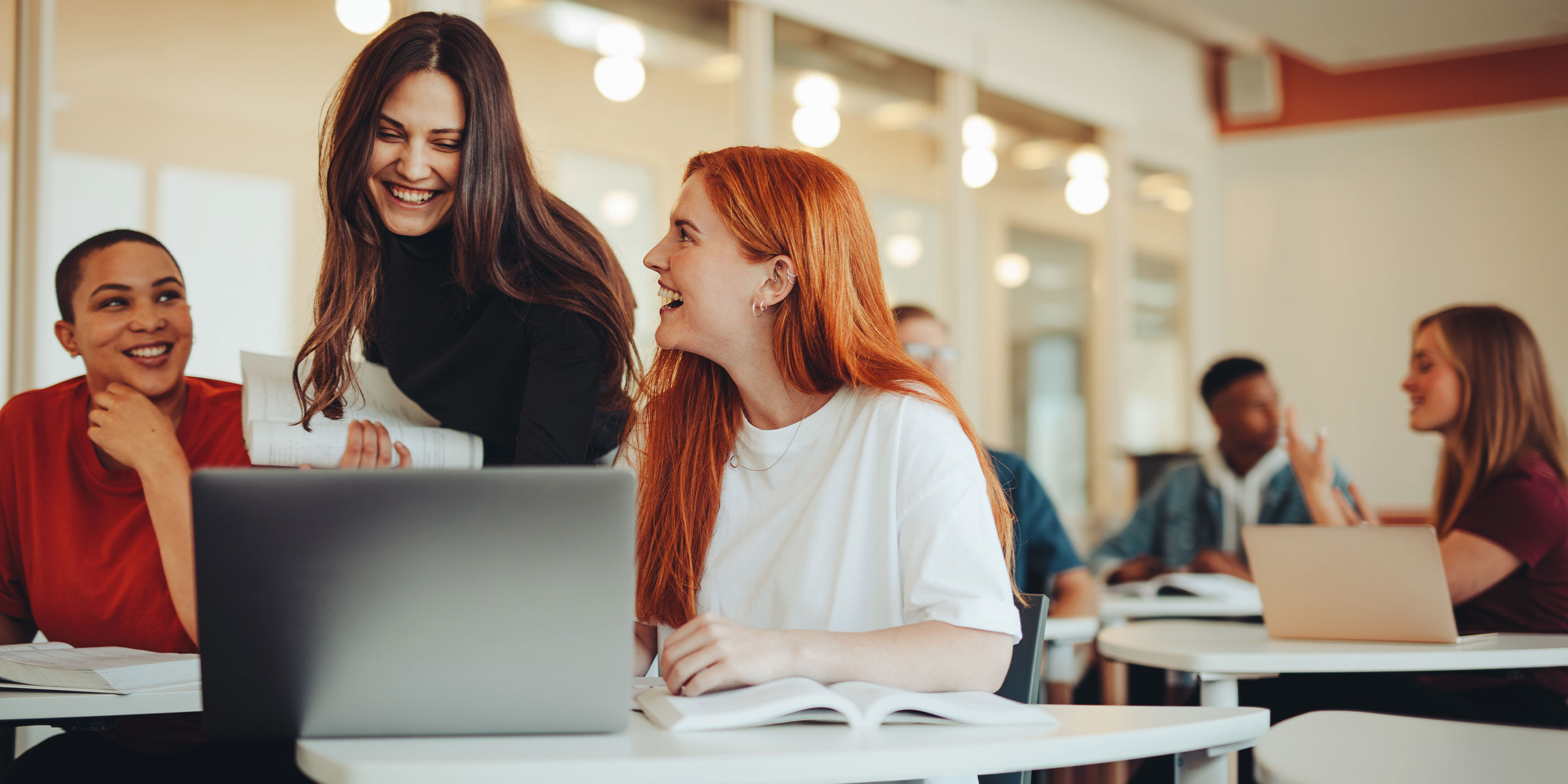 Verschiedene Personen sitzen an Schreibtischen und arbeiten mit Laptops.