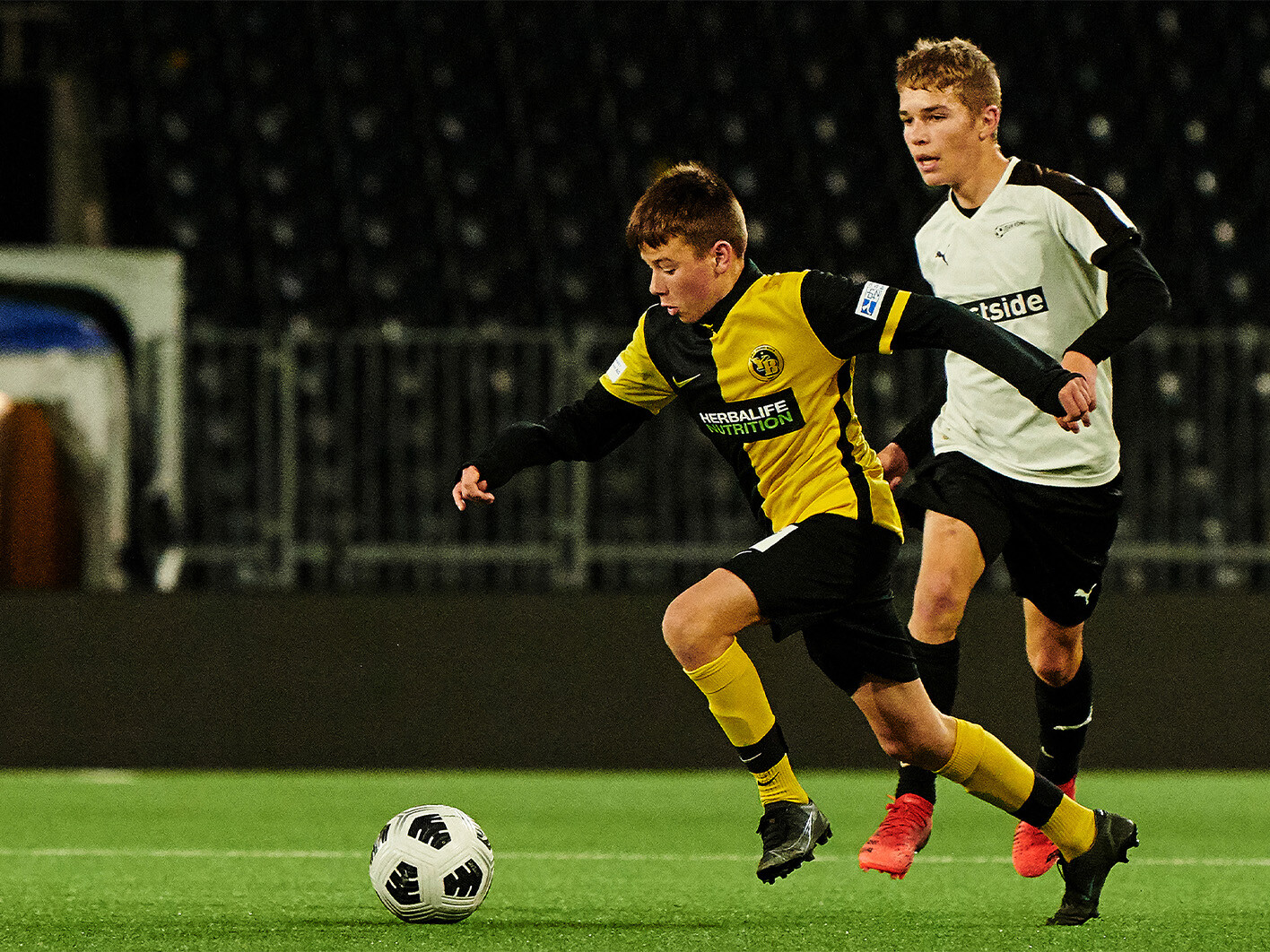 Ein Fussballspieler in einem gelb-schwarzen Trikot und ein Fussballspieler in einem weiss-schwarzen Trikot kämpfen um den Ball.