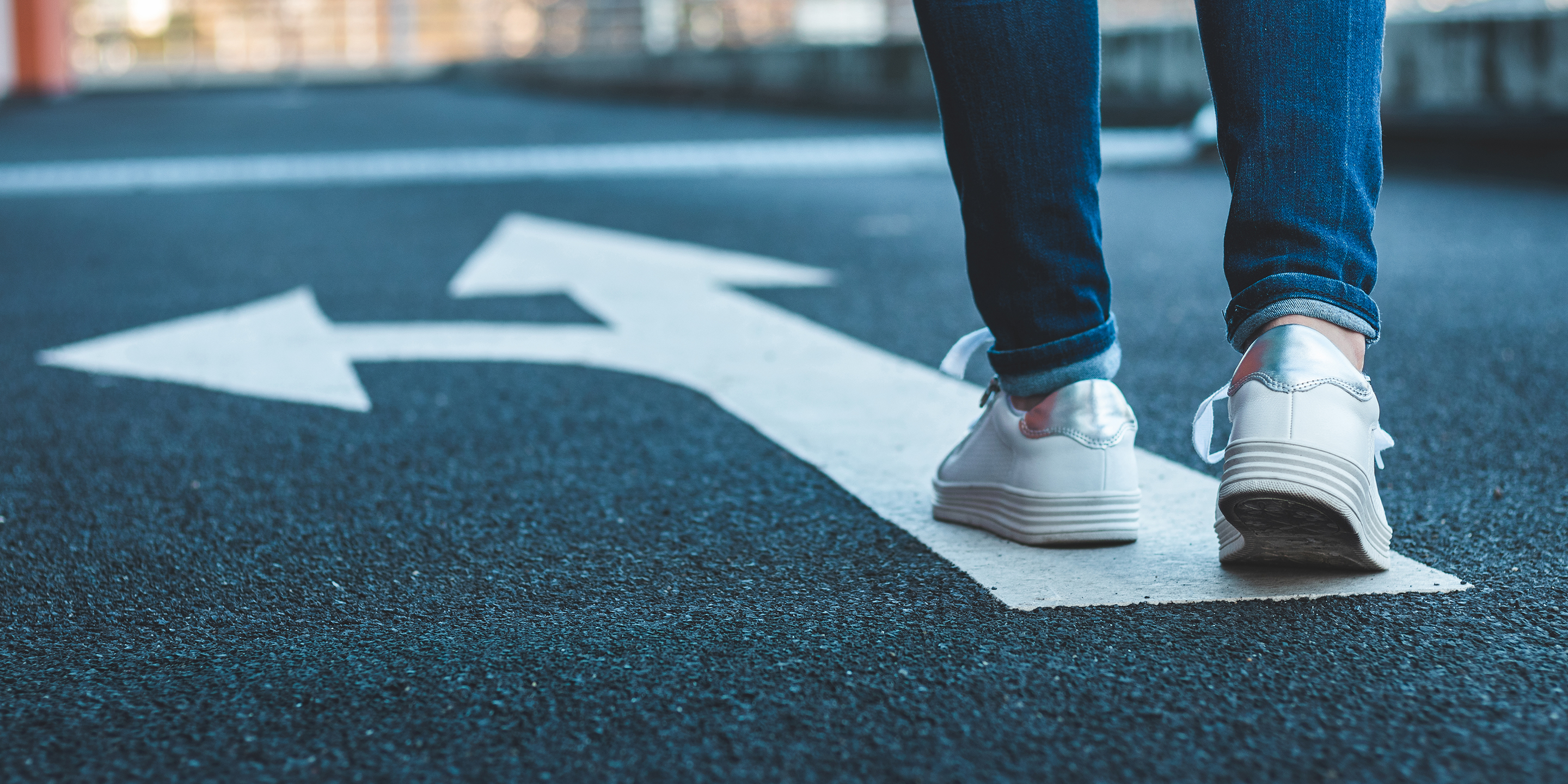 Zwei Füsse in weissen Turnschuhen auf einem weissen Pfeil