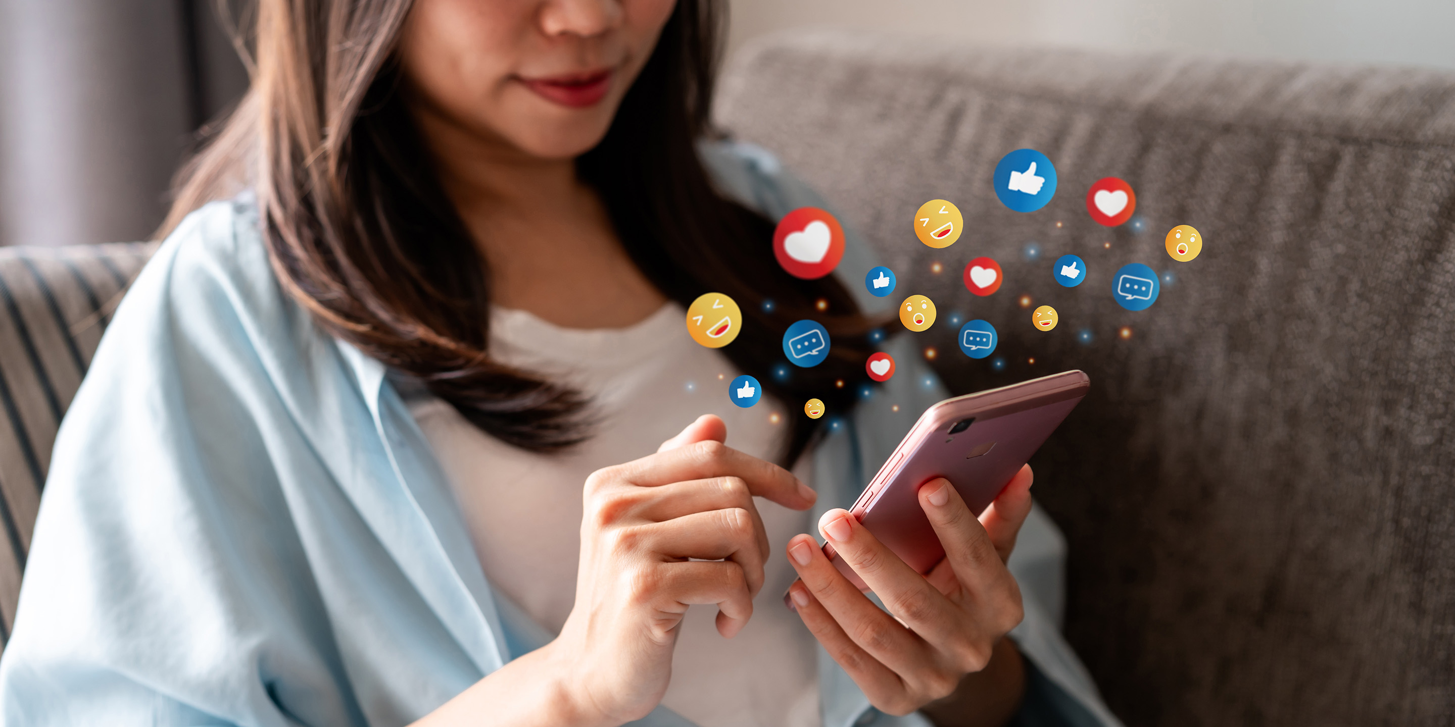 Eine Person hält eine Handy in der Hand. Verschiedene Emojis schweben über dem Handy.