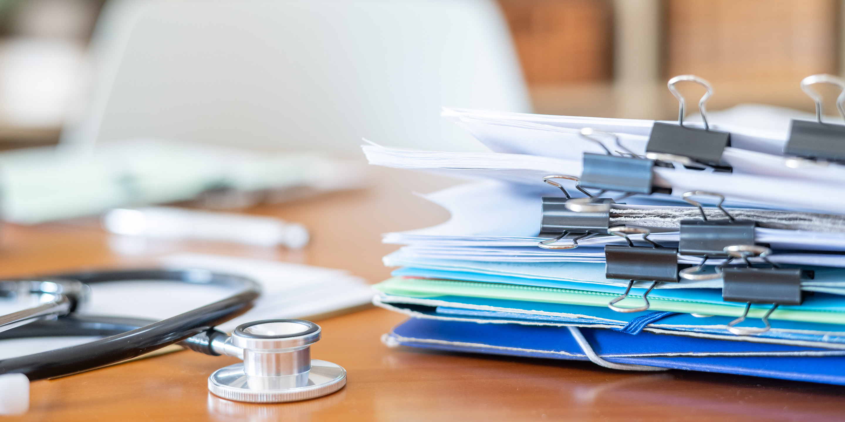 Stethoskop und Patientenakten auf einem Schreibtisch in einer medizinischen Praxis.