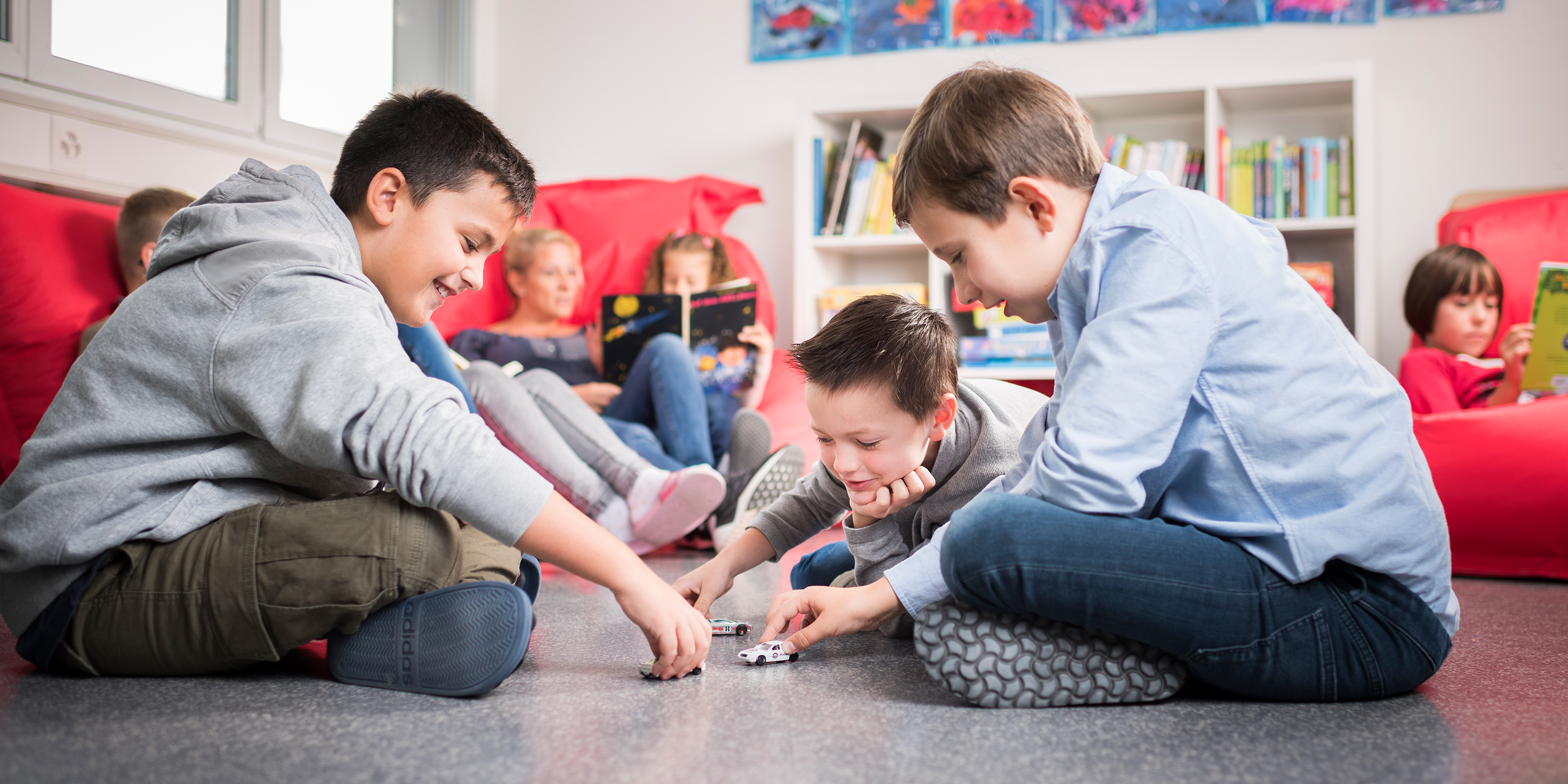 Kinder sitzen am Boden oder auf Sesseln.