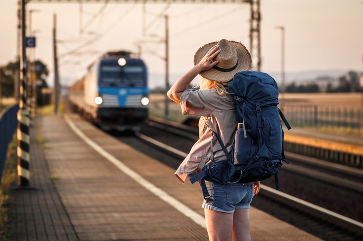 Eine Person mit Rucksack steht auf einem Perron. Ein Zug fährt ein.