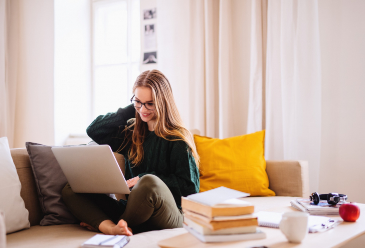 Eine Frau sitzt auf einem Sofa und arbeitet mit einem Laptop.