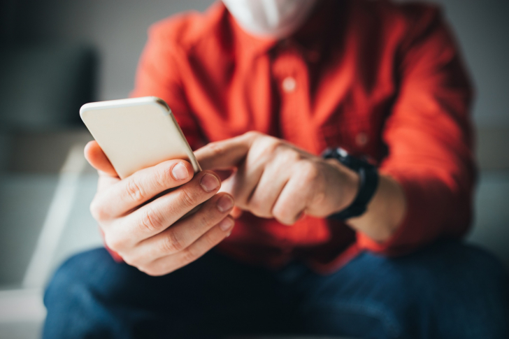 Mann in orangem Hemd mit Handy in der Hand