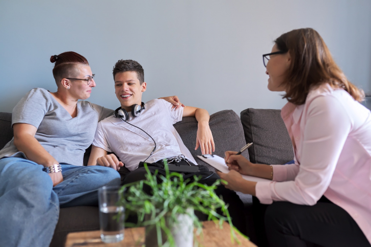 Drei Personen sitzen auf einem Sofa.