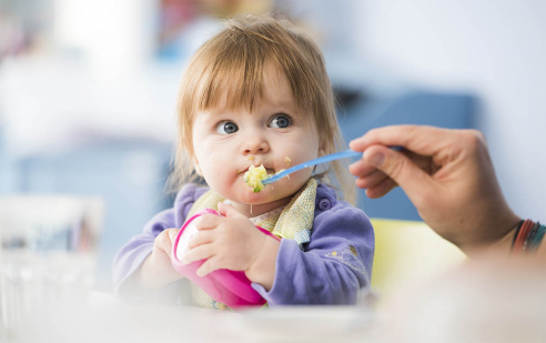 Ein Kind in der Feusi Kita Kindertagesstätte in Muri-Gümligen wird mit mit einer Hand, die einen Löffel hält, gefüttert.