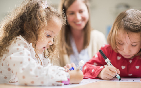 Zwei Mädchen in der Feusi Preschool in Muri-Gümligen zeichnen und malen unter der Aufsicht einer Lehrerin. 