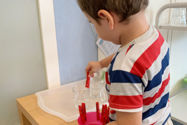 A child puts clothespins on a glass.