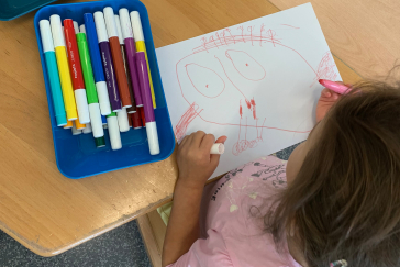 A child sits at a table and draws with different crayons.