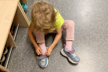 A child sits on the floor and closes his shoes.