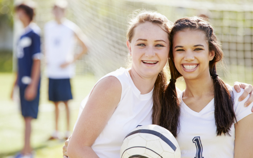 10. Schuljahr Sport.in Bern. Zwei lachende Mädchen halten einem Fussball.