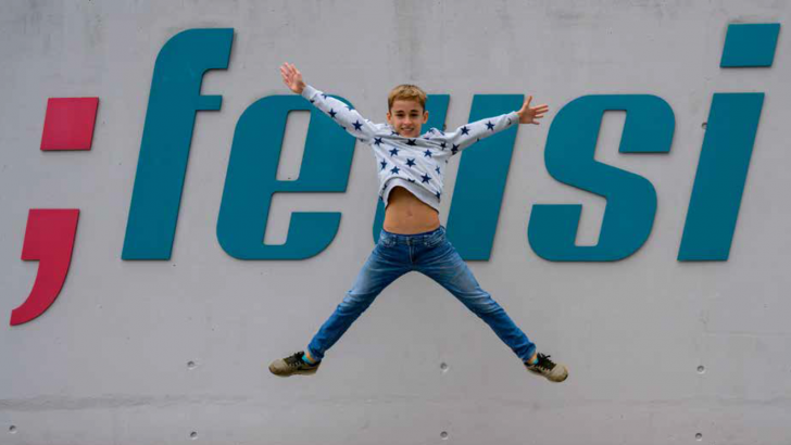 Ein Junge springt vor der Wand mit dem Feusi Logo in die Luft
