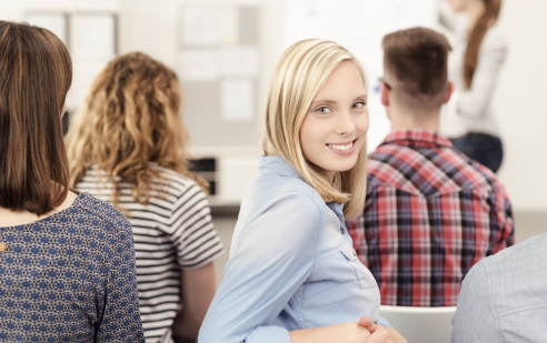 Human Resources am Feusi Bildungszentrum. Eine lächelnde junge Frau sitzend und weitere Personen Rückenansicht sitzend.